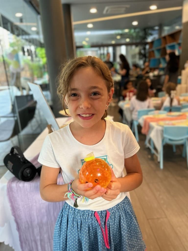 Smiling girl holding the orange glitter squishy she made at a Glello party